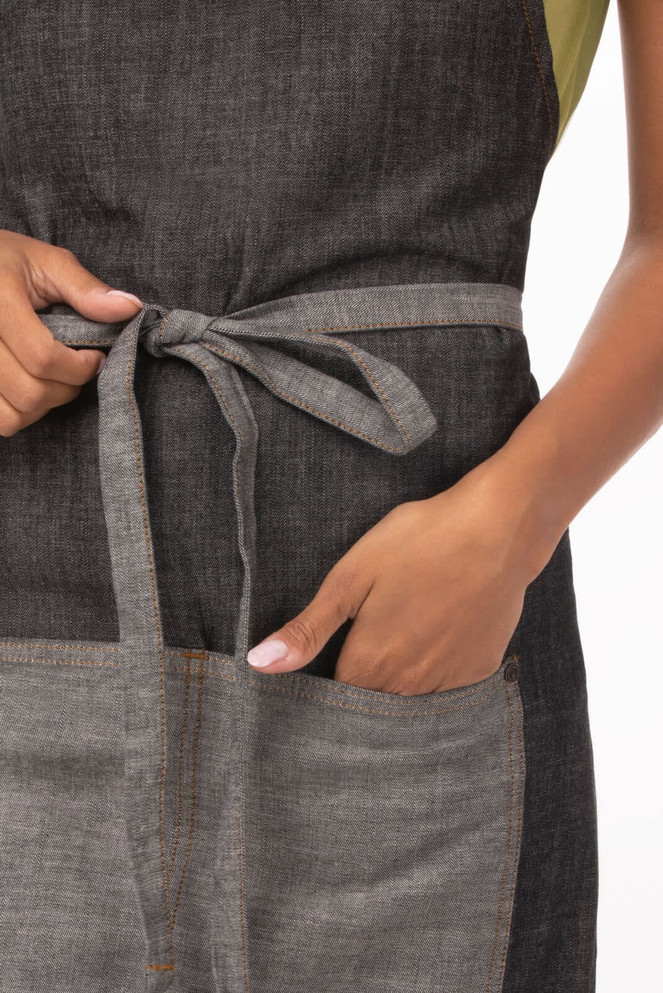 A grey Manhattan Bib Apron with a tied waist and a front pocket, featuring a subtle textured fabric.