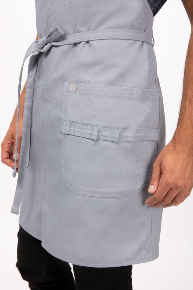 A light grey bib apron featuring a front pocket and a tie belt, part of the workwear collection.