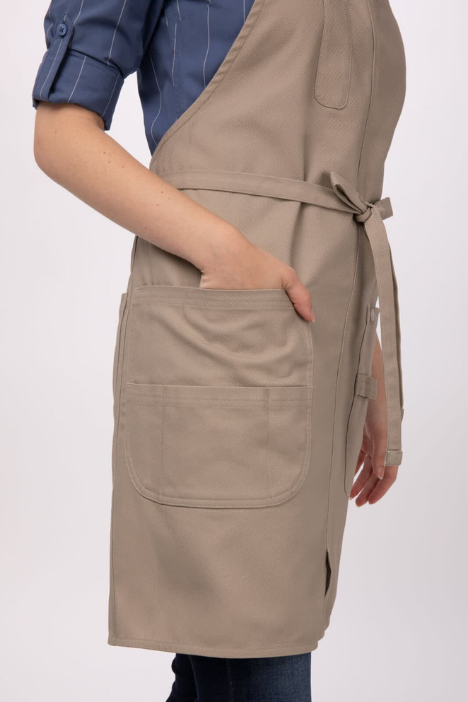 A beige Logan Bib Apron featured on a model, with two front pockets and adjustable straps.
