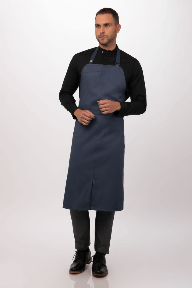 A dark blue bib apron is worn by a model, featuring a simple design and adjustable straps. It includes a logo.