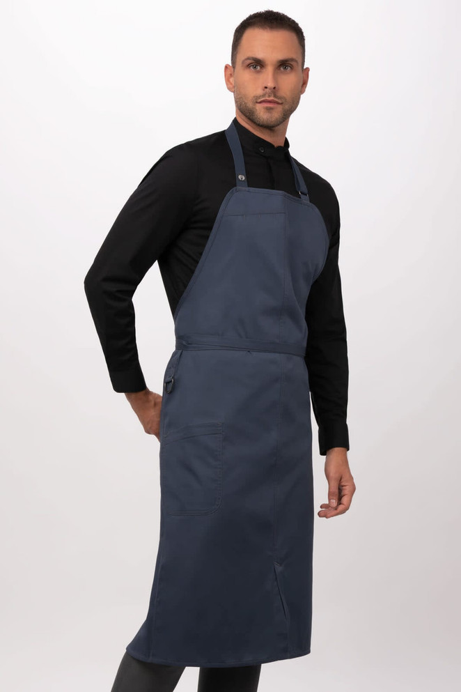 A dark blue bib apron worn by a model, featuring adjustable straps and a logo.