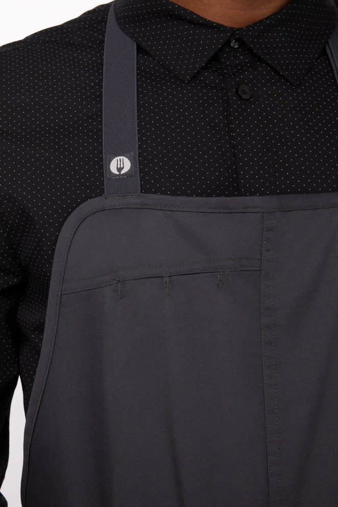 A grey Brio Chef Bib Apron with a pocket and a logo, worn over a dotted black shirt.
