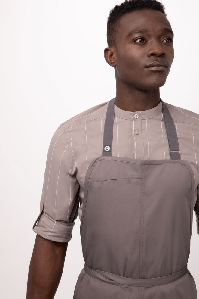 A man in a grey Brio Chef Bib Apron over a striped shirt, featuring adjustable straps and a logo.