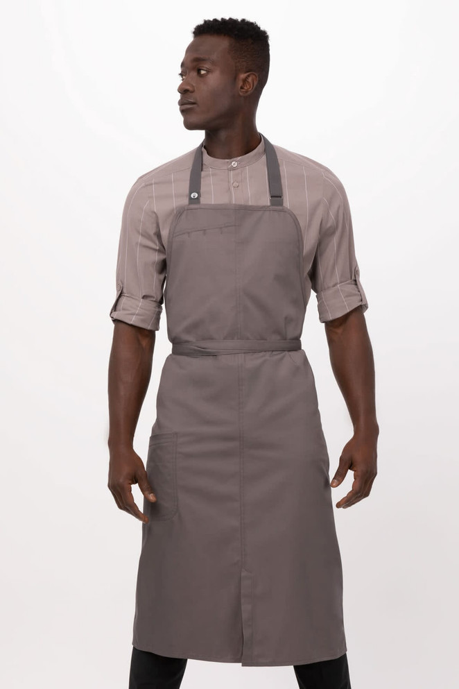 A grey bib apron with adjustable straps, worn by a model. The apron has a simple design and includes a logo.