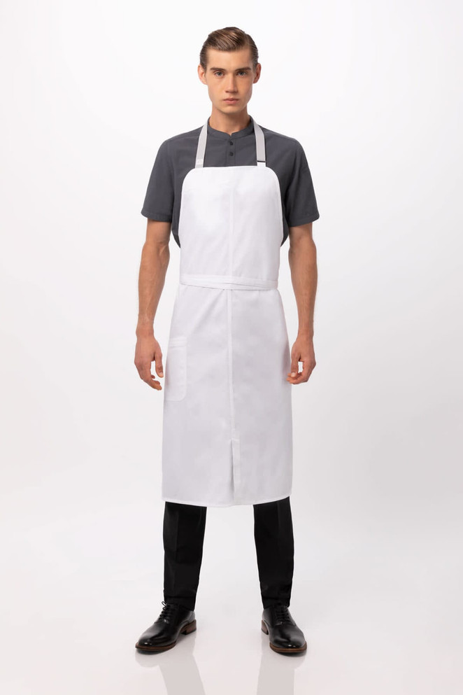 A white bib apron worn by a model, featuring a simple design and adjustable straps. The model is dressed in black trousers and shoes.