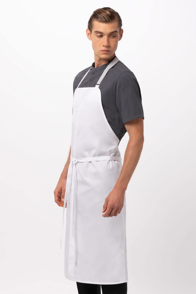 A white bib apron worn by a model, featuring a simple design and adjustable ties. It has a logo on it.