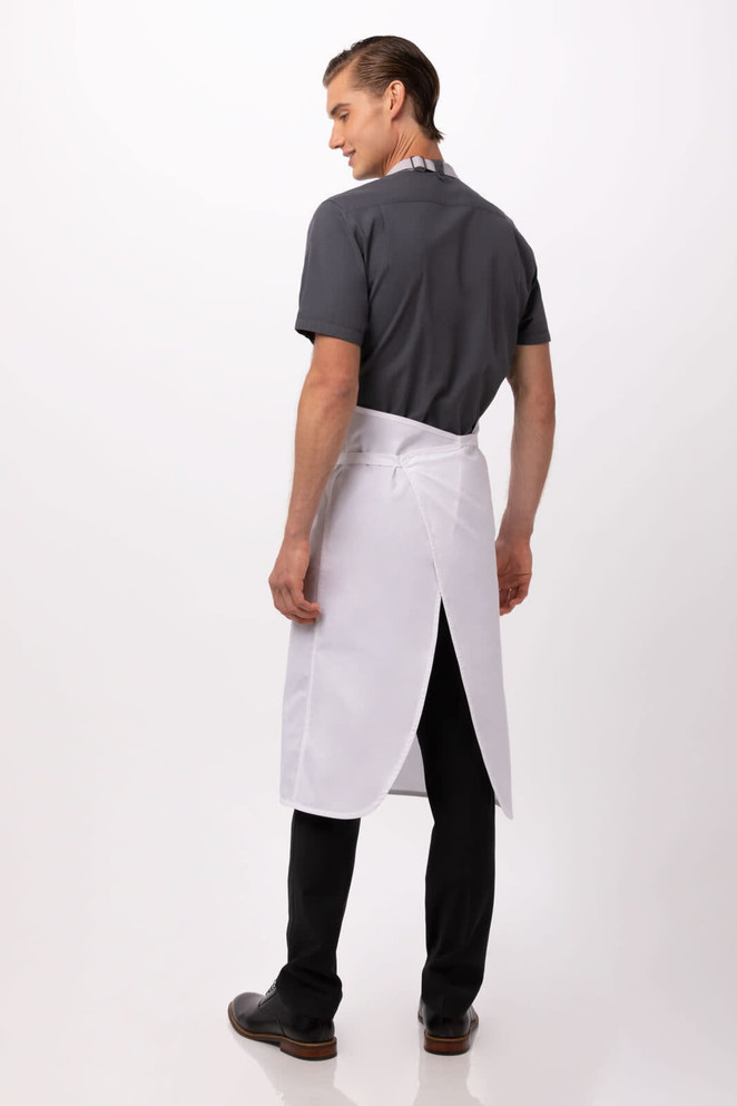 A man wearing a white bib apron over a grey shirt, viewed from the back with black trousers and shoes.