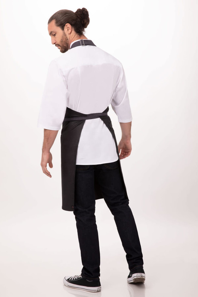 A man wearing a black Boulder Bib Apron over a white shirt and jeans, standing with his back to the camera.