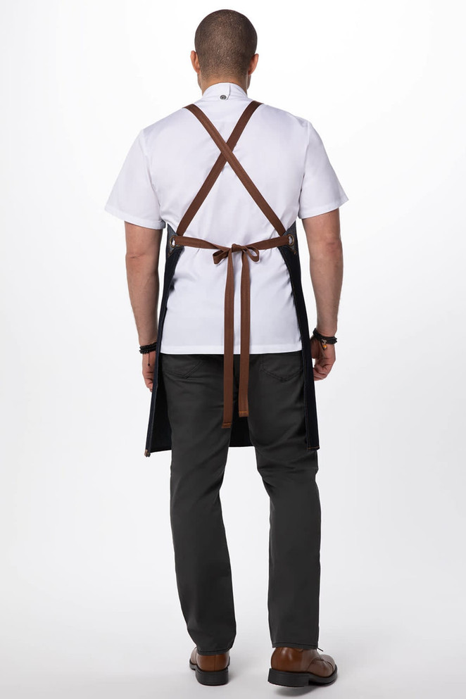 A cross back apron in denim with brown straps, worn by a person facing away, showcasing its design and colour.