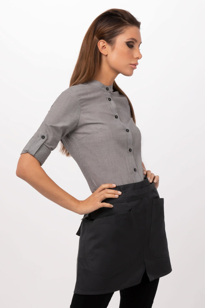 A woman wearing a grey top and a black half bistro apron, featuring pockets and buttons. The apron has a logo.