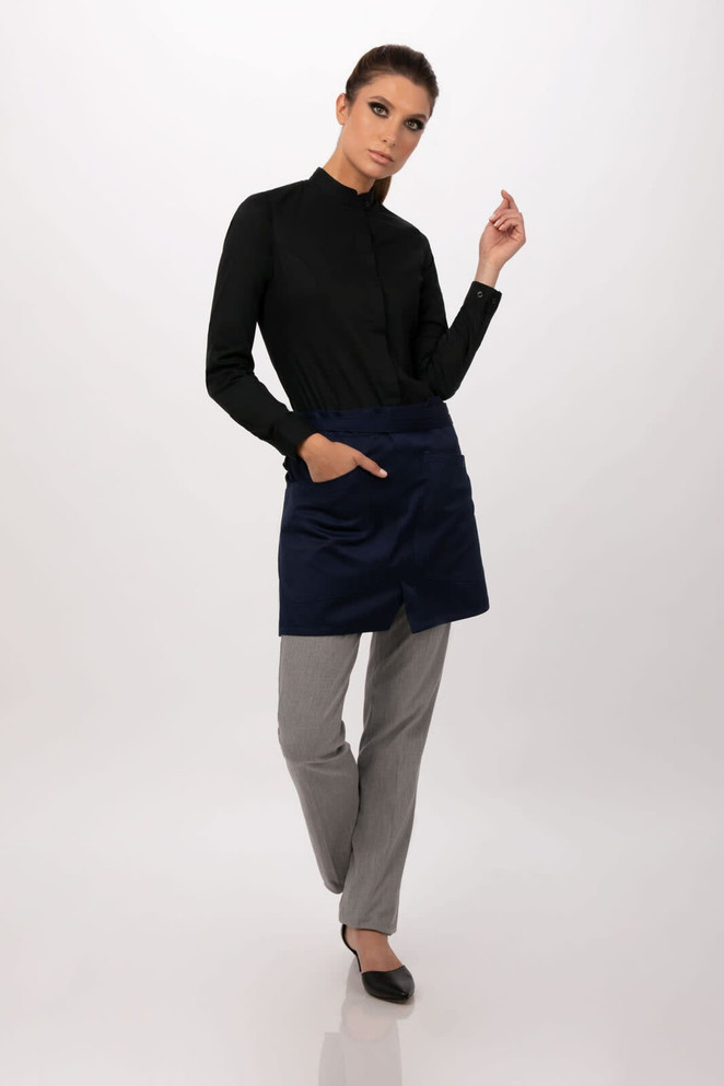 A model wears a navy half bistro apron over grey trousers, with a black long-sleeve shirt and stylish black shoes.