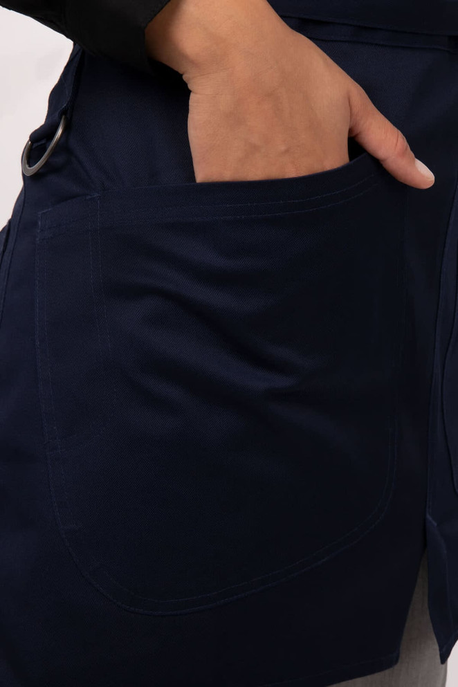 A navy half bistro apron featuring a side pocket, showcasing a hand reaching into the pocket.