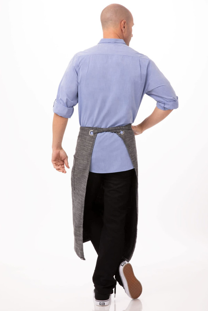 A grey bistro apron is worn over black trousers and a blue shirt, showcasing a back view of the outfit.
