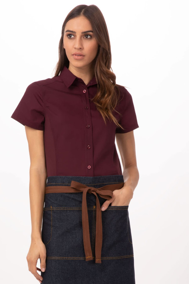 A woman models a maroon shirt paired with a denim apron featuring a brown tie belt. The apron has a simple design.