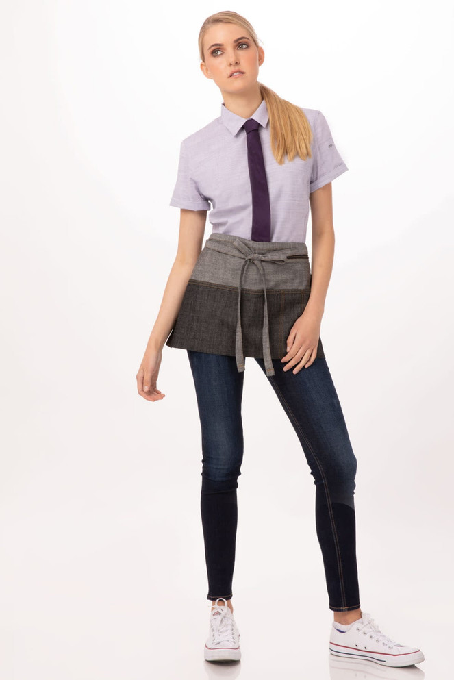 A person wearing a grey waist apron over a shirt and jeans, with a logo visible on the apron.