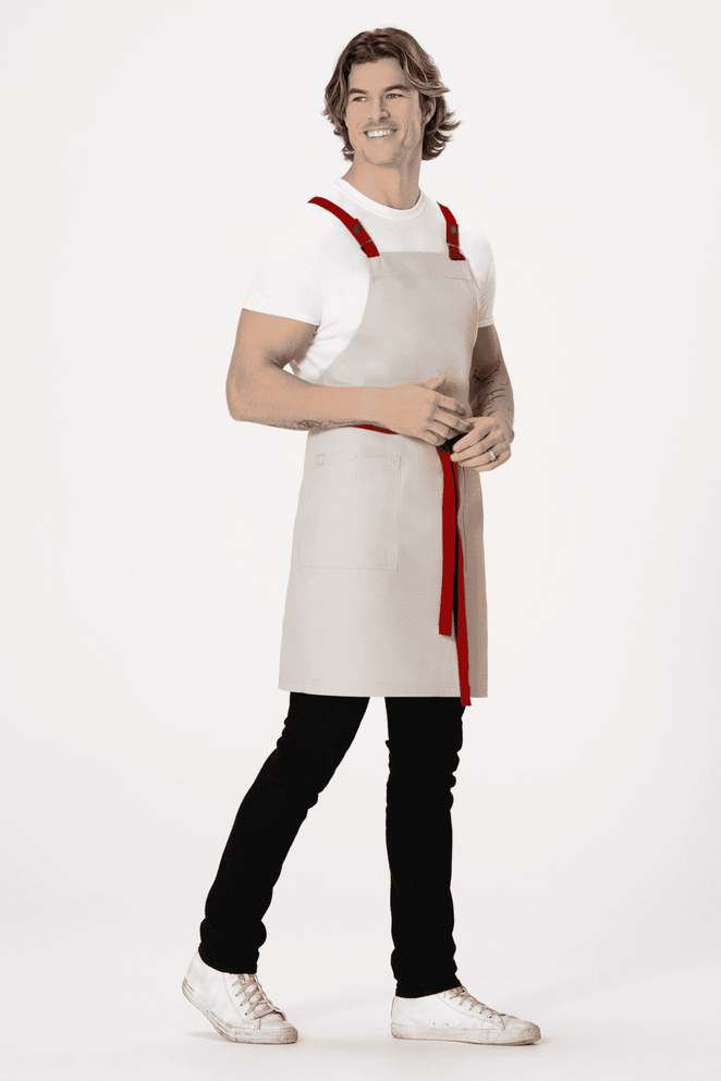 A grey cross-back apron with red straps displayed on a model wearing a white shirt and black pants.