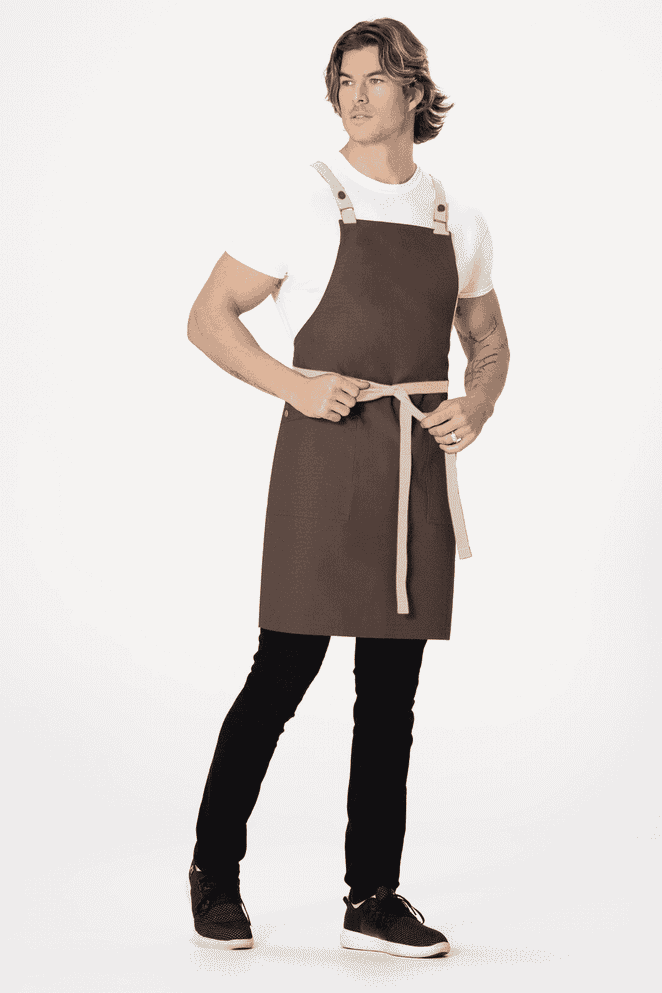 A brown cross back apron with adjustable straps and a waist tie, worn by a model against a plain background.