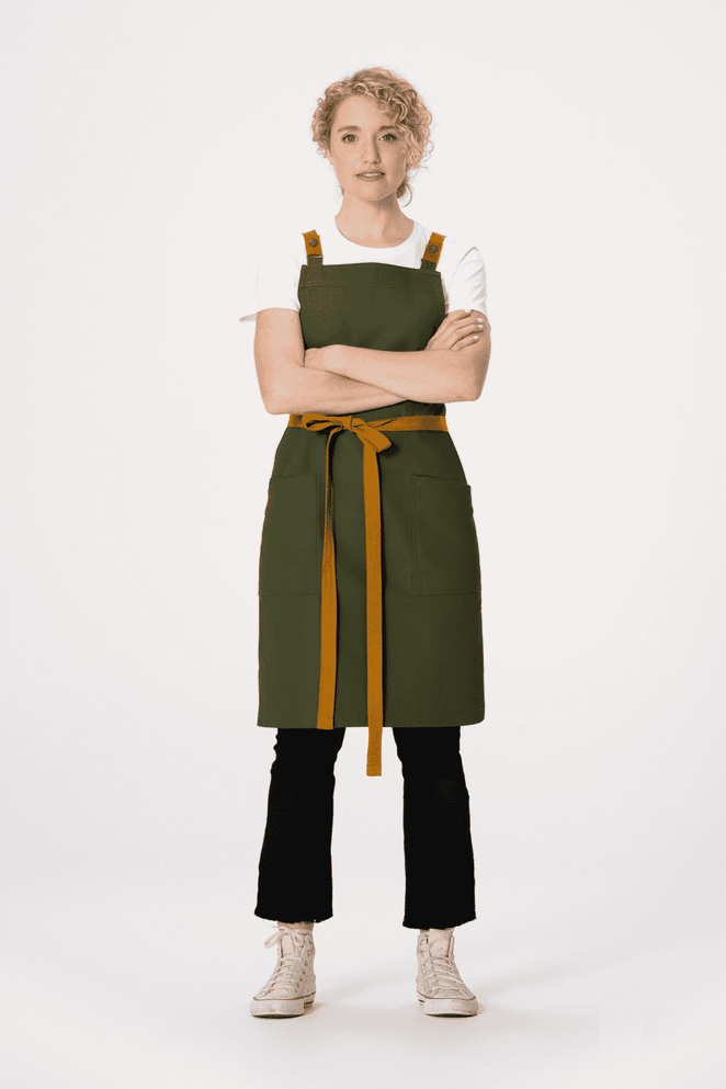 A green cross back apron with a brown tie, worn over a white shirt and black pants, featuring a logo.