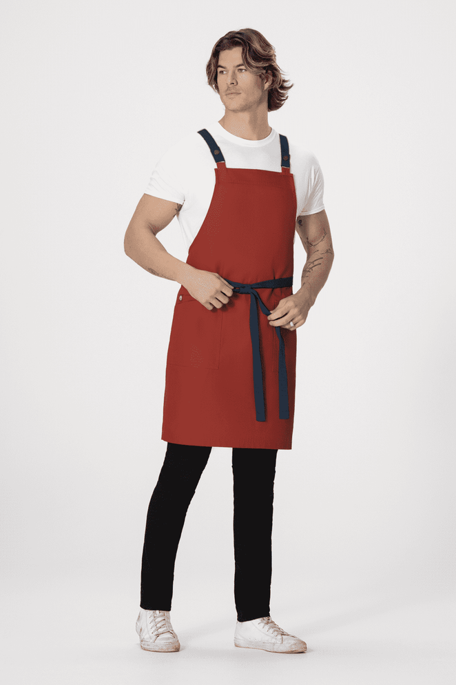 A red Lockharte cross back apron with adjustable straps and a waist tie is worn by a model.