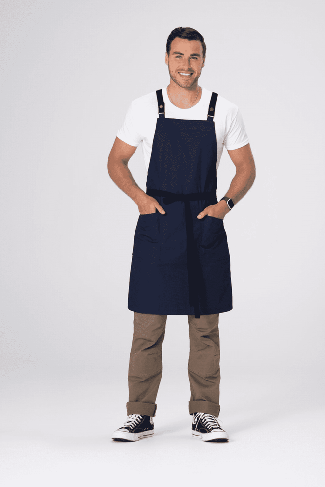 A navy blue cross back apron featuring adjustable straps and front pockets, modelled by a smiling man.