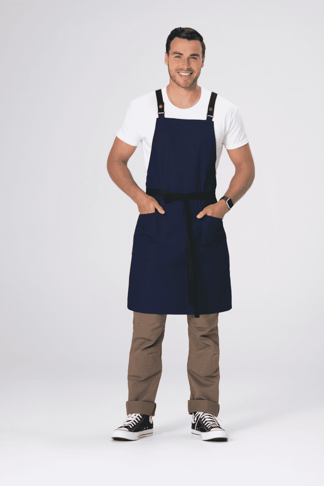A man wearing a navy blue cross back apron with front pockets and a black tie waist.