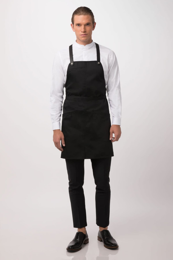 A black Largo Bib Apron is worn by a model, paired with a white shirt and black trousers. The apron features straps and has a logo.