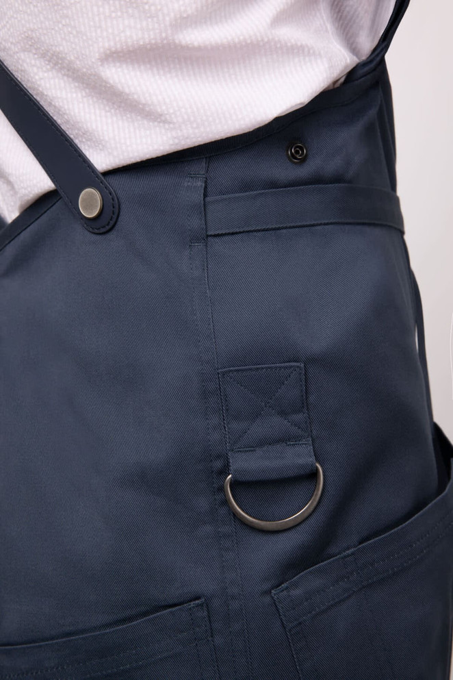 A navy blue Largo Bib Apron featuring a side pocket with a metal ring and adjustable straps.
