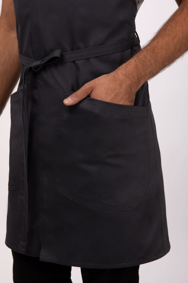 A dark grey bib apron with a pocket, featuring a tie waist and a simple design. It has a logo present.