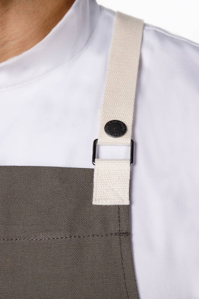 A grey Byron Cross-Back Apron featuring a cream-coloured strap and a black fastener. Includes a branding logo.