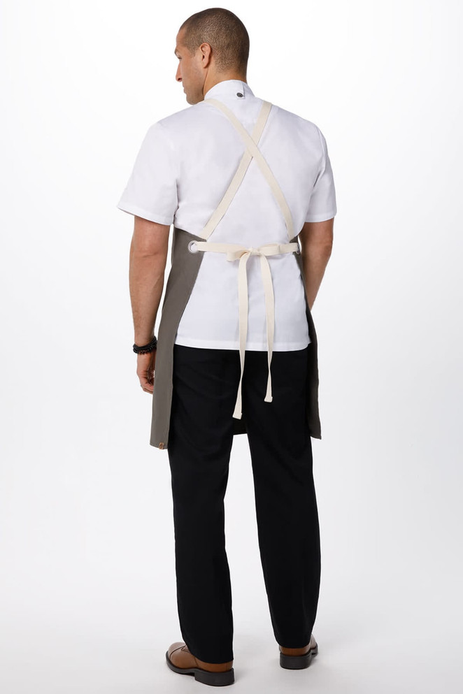 A man wearing a grey Byron Cross-Back Apron over a white shirt, showcasing an adjustable strap design.