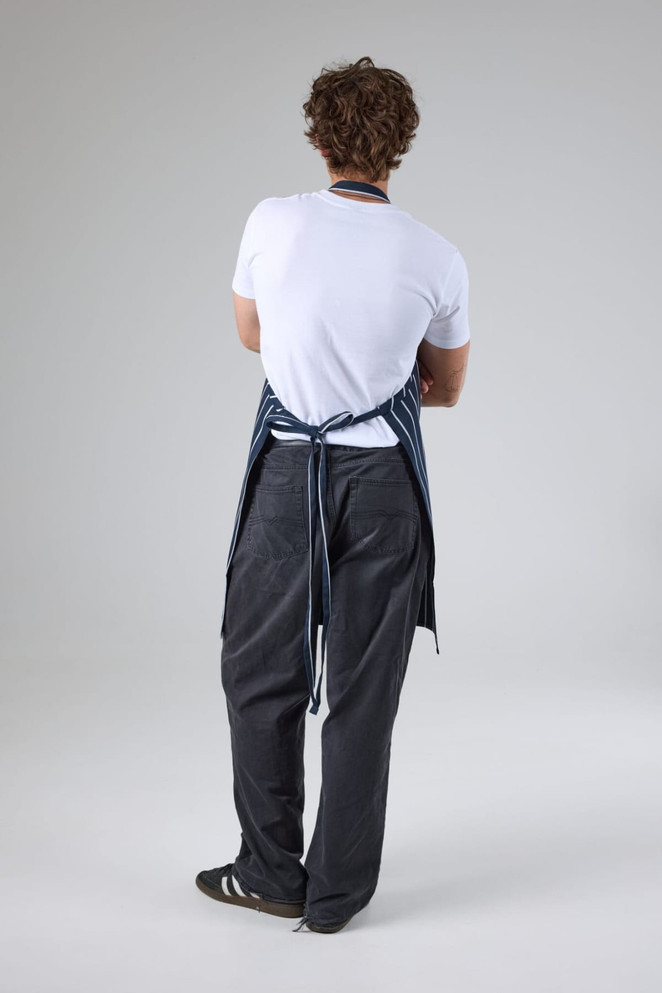 A blue and white striped bib apron worn by a person facing away, paired with grey pants and black shoes.
