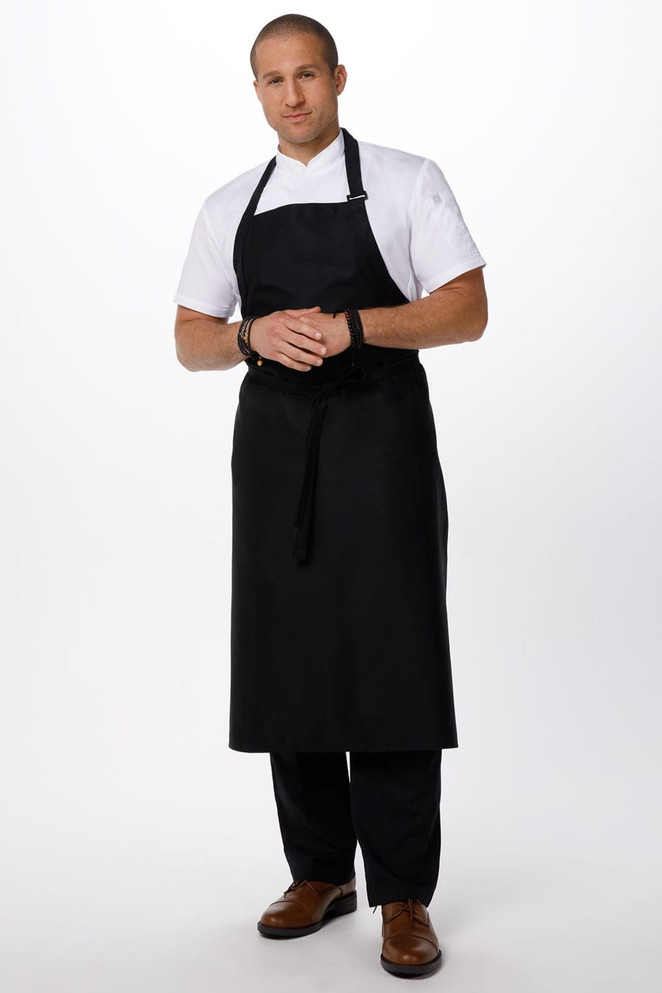 A black large bib apron worn by a model in a white shirt and black pants, featuring a logo on the apron.