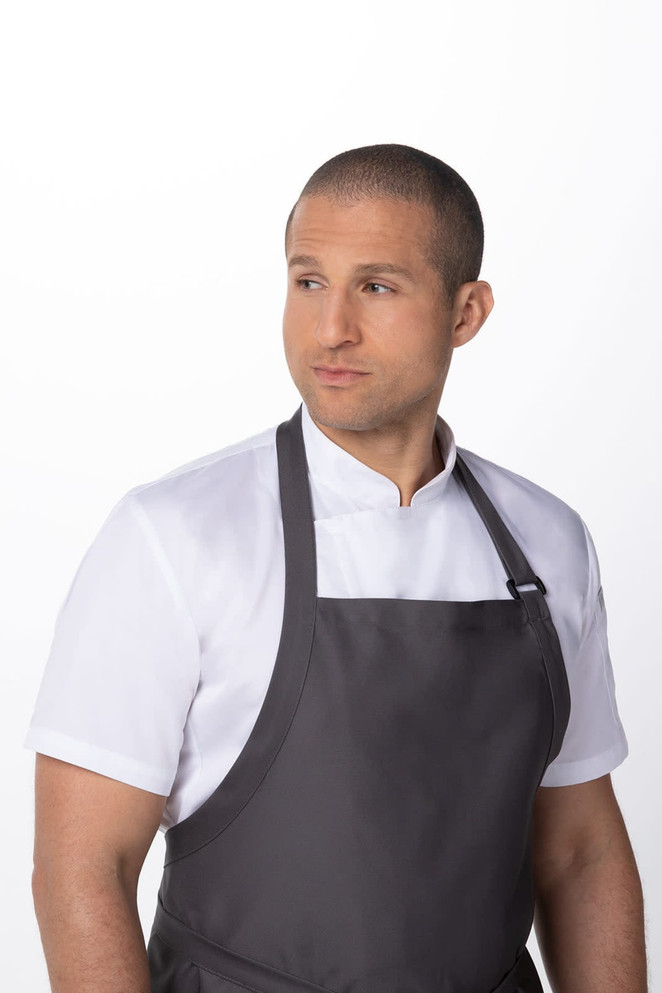 A man wearing a grey large bib apron over a white shirt, featuring a simple design and a logo.