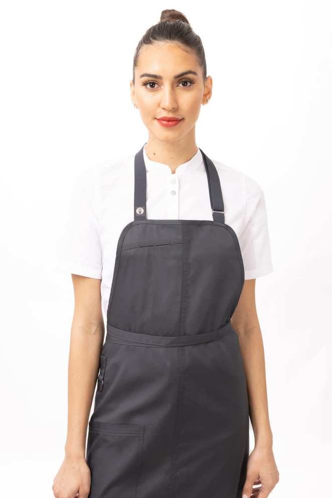 A woman wearing a black Brio Bib Apron over a white shirt, featuring a logo on the apron.