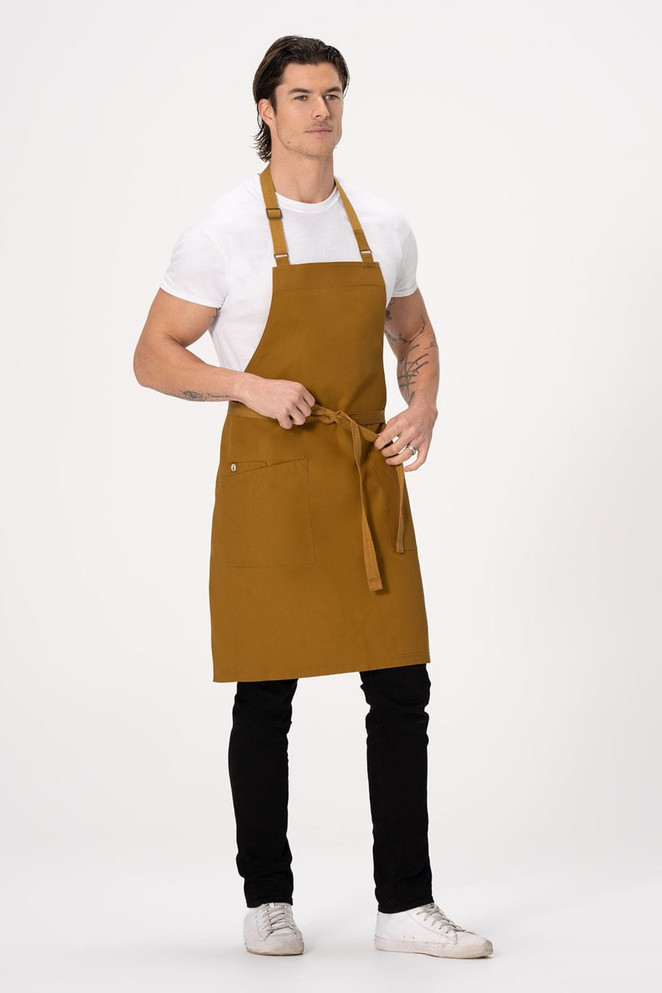 A brown bib apron with adjustable straps, featuring a pocket, worn by a model standing and tying the waist.