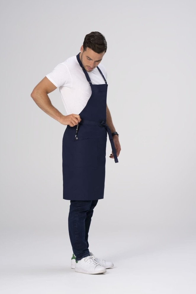 A man wearing a navy blue Lockharte bib apron over a white shirt and jeans, featuring a logo.