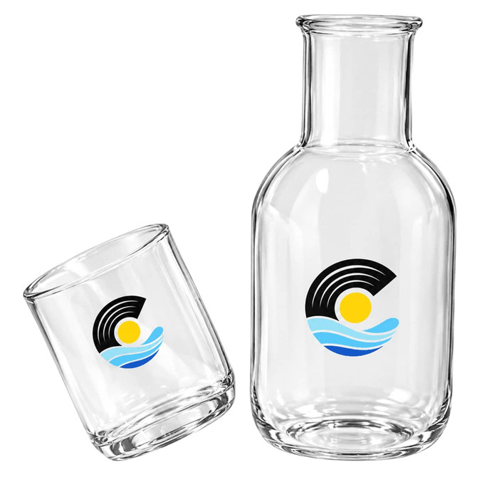 A glass carafe and cup set in clear glass, featuring a logo, with a sleek design.