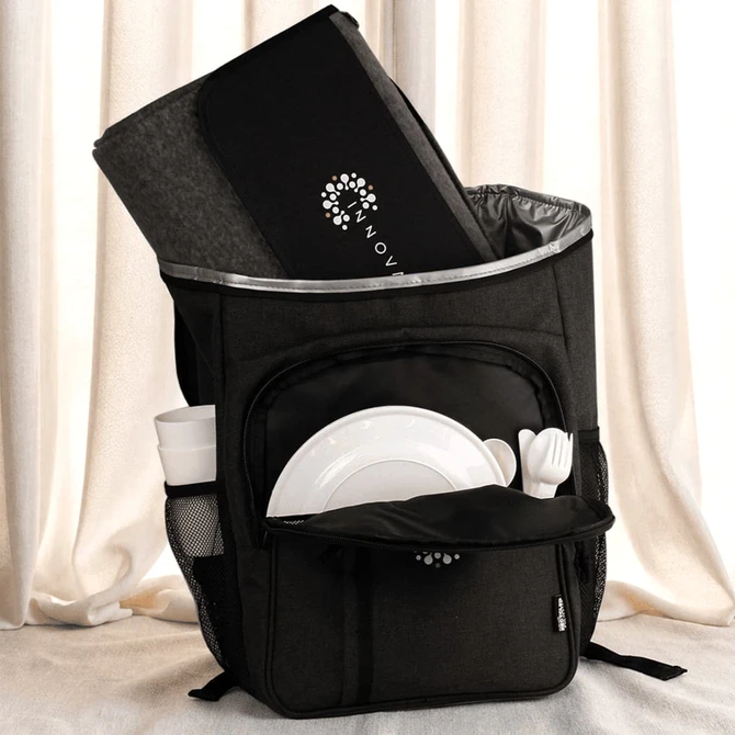 A black picnic backpack with a grey blanket, plates, cutlery, and a drink bottle in external pockets.