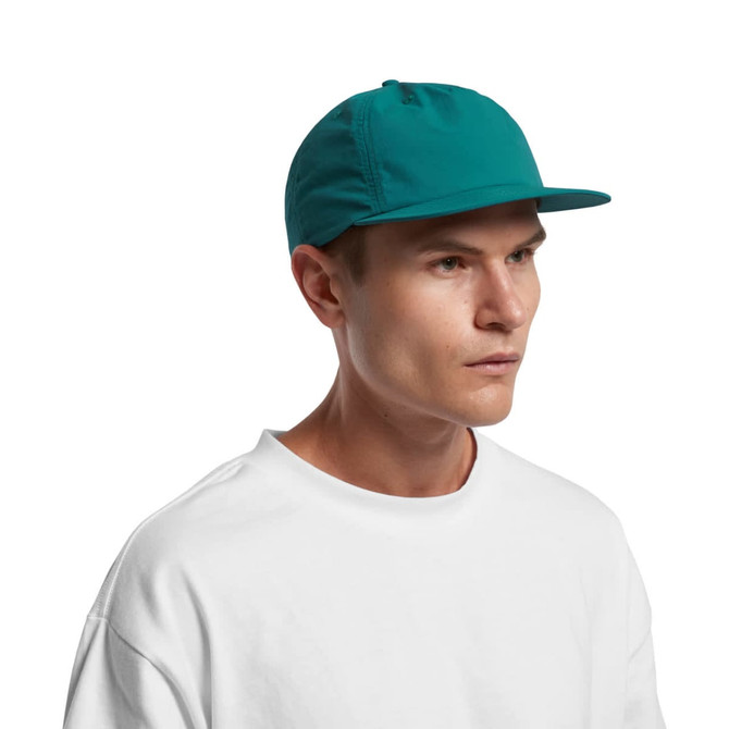 A teal cap with a flat brim and a branded logo on the front, worn by a model in a white shirt.
