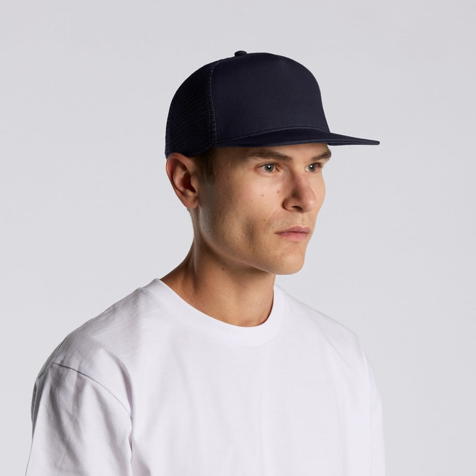 A navy trucker cap with a flat brim, featuring a logo, worn by a model in a white T-shirt.