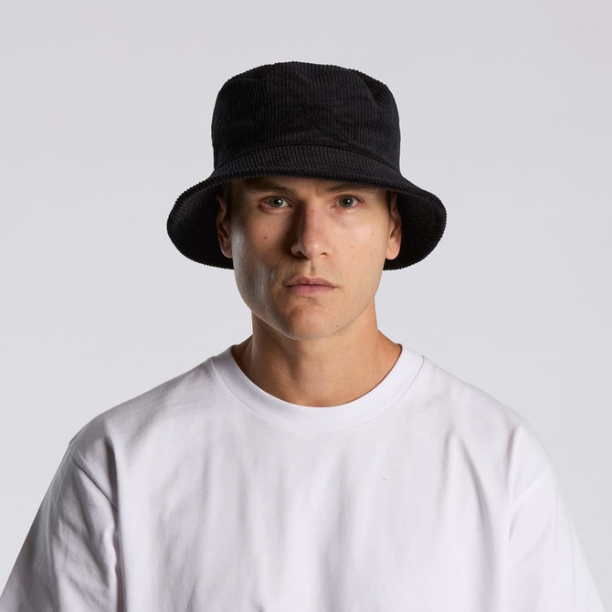 A black cord bucket hat worn by a model, paired with a plain white t-shirt. The hat features a branding logo.