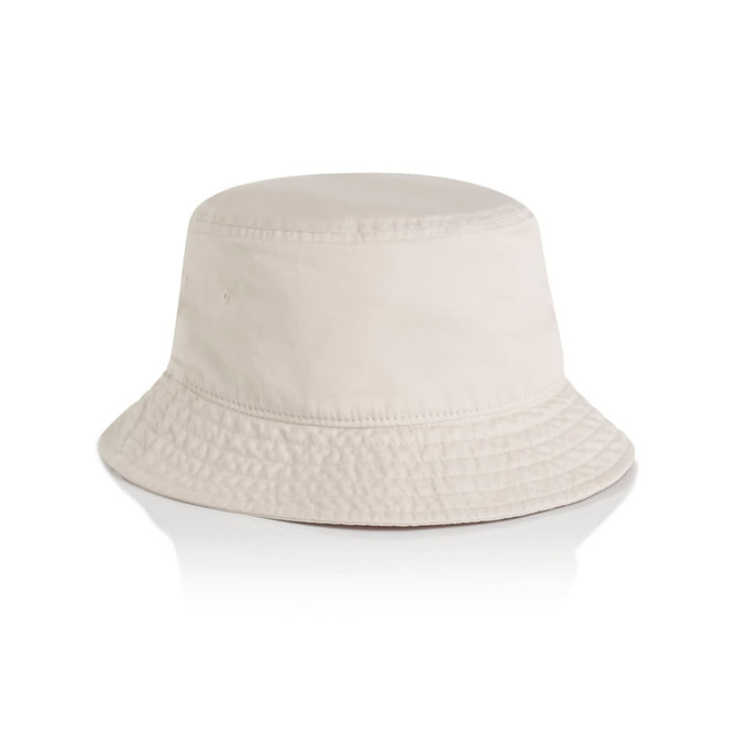 A faded cream bucket hat featuring a textured appearance and a wide brim. It has a branding logo on the side.