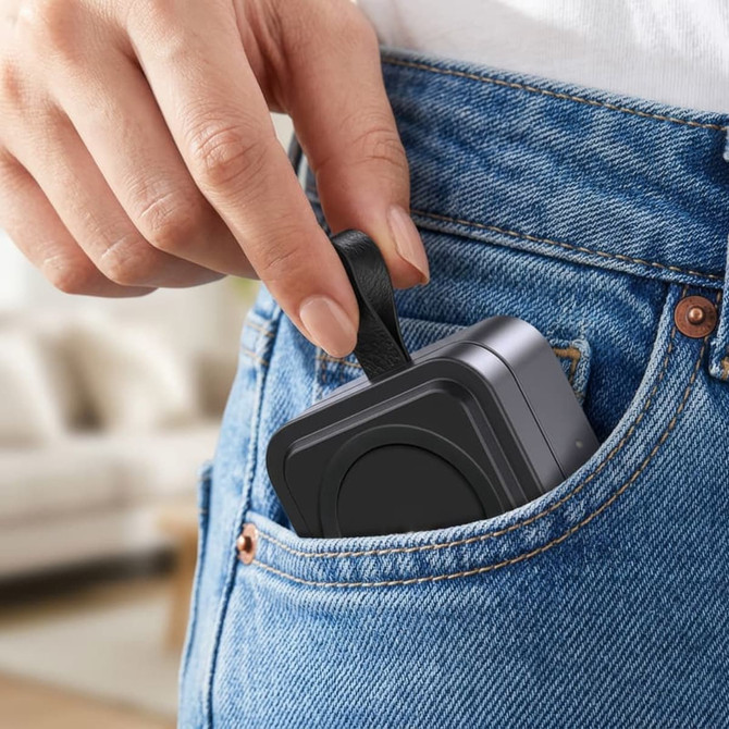 A compact grey magnetic wireless charging station being placed in a pocket of denim jeans.