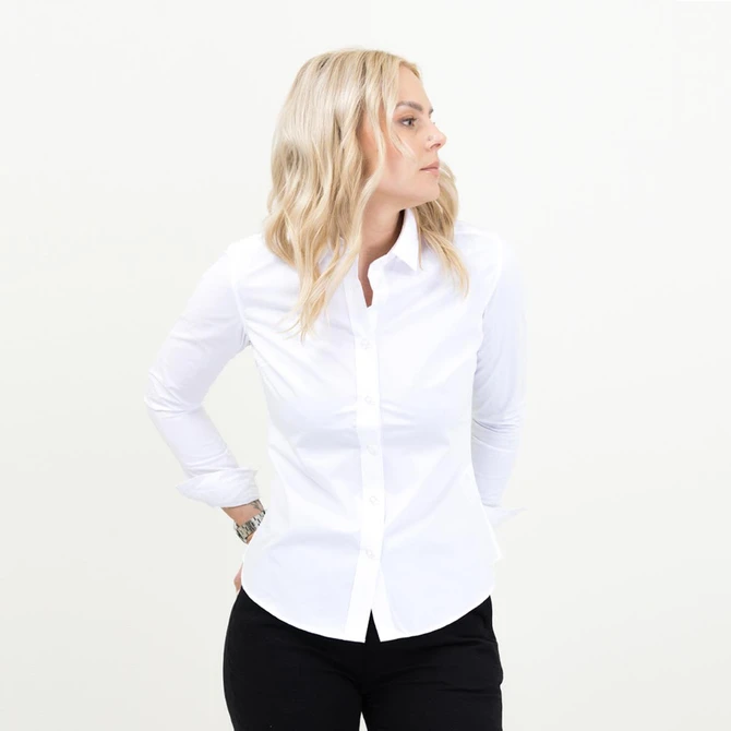 A white women's shirt with long sleeves and a button-up front, worn with black trousers. The model stands facing sideways.