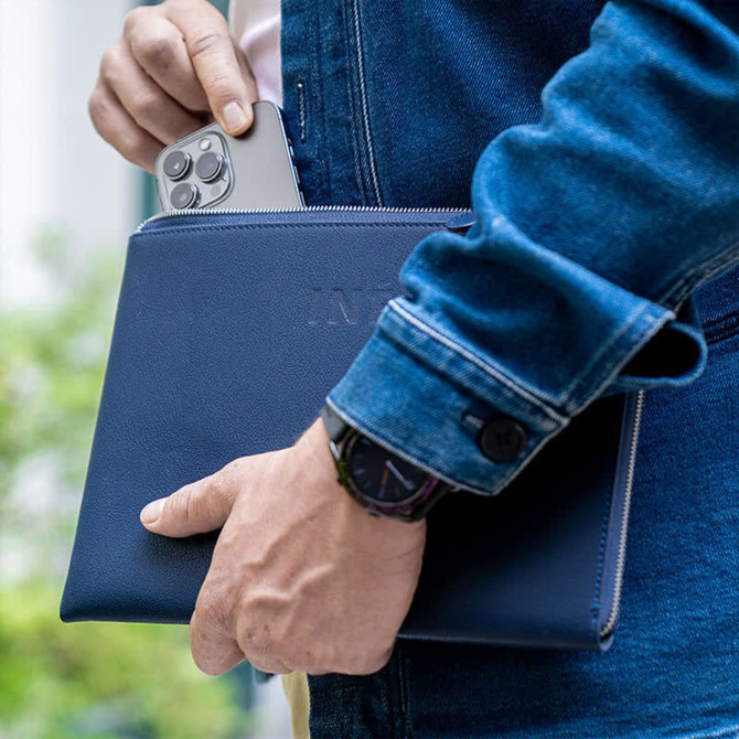 A navy tablet case is held by a person, with a smartphone partially visible inside the case. The image features a logo.