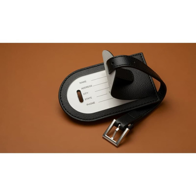 A black luggage tag made of recycled leather, featuring a silver buckle and a white card for personal information.