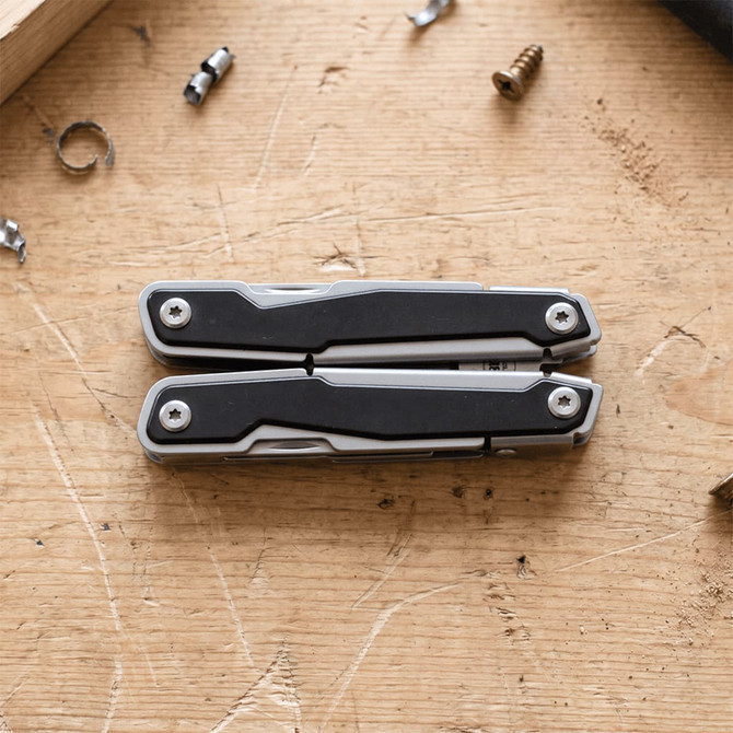 A silver and black multifunction tool displayed on a wooden surface, surrounded by small screws and metal fragments.