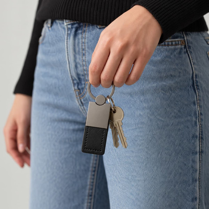 A hand holds a black and silver keytag attached to a keyring, alongside several keys.