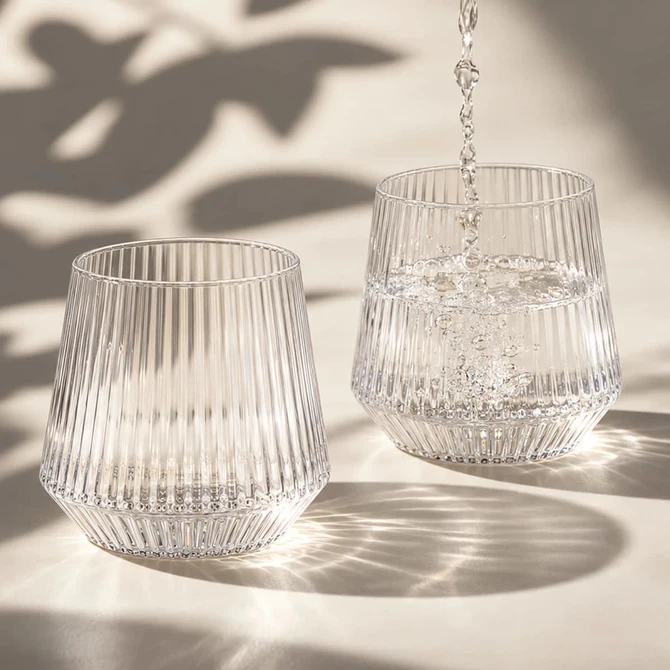 A drink bottle featuring a ribbed design, made of clear glass, with water being poured into two glasses.