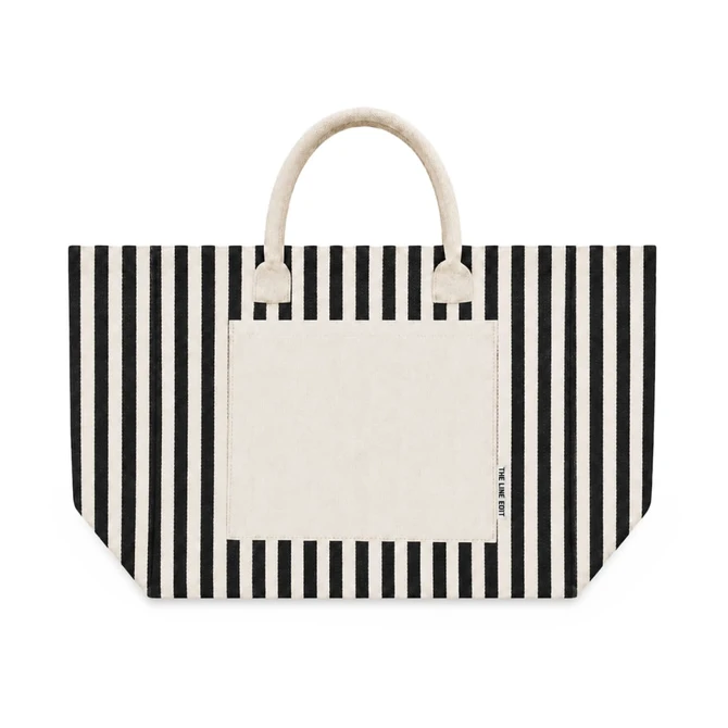 A striped tote bag featuring black and cream colours, with a solid cream pocket and handles. It has a brand logo.